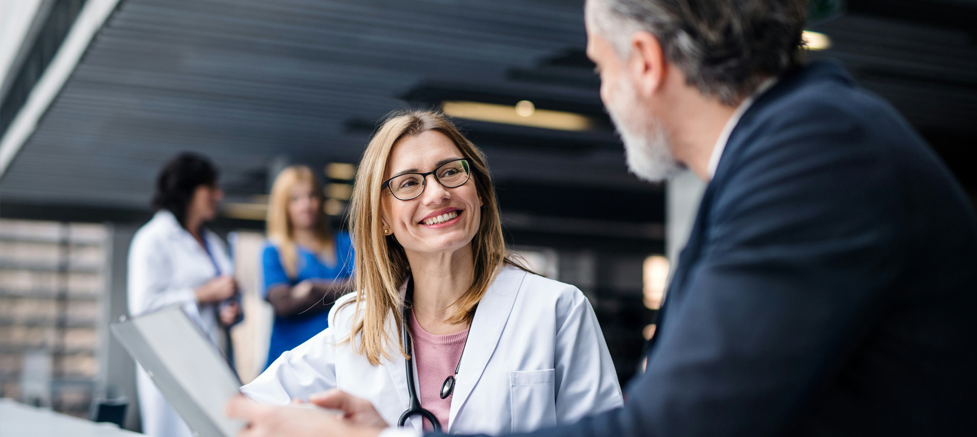 Female doctor smiles as she speaks to a male in a suit in the hospital hallway